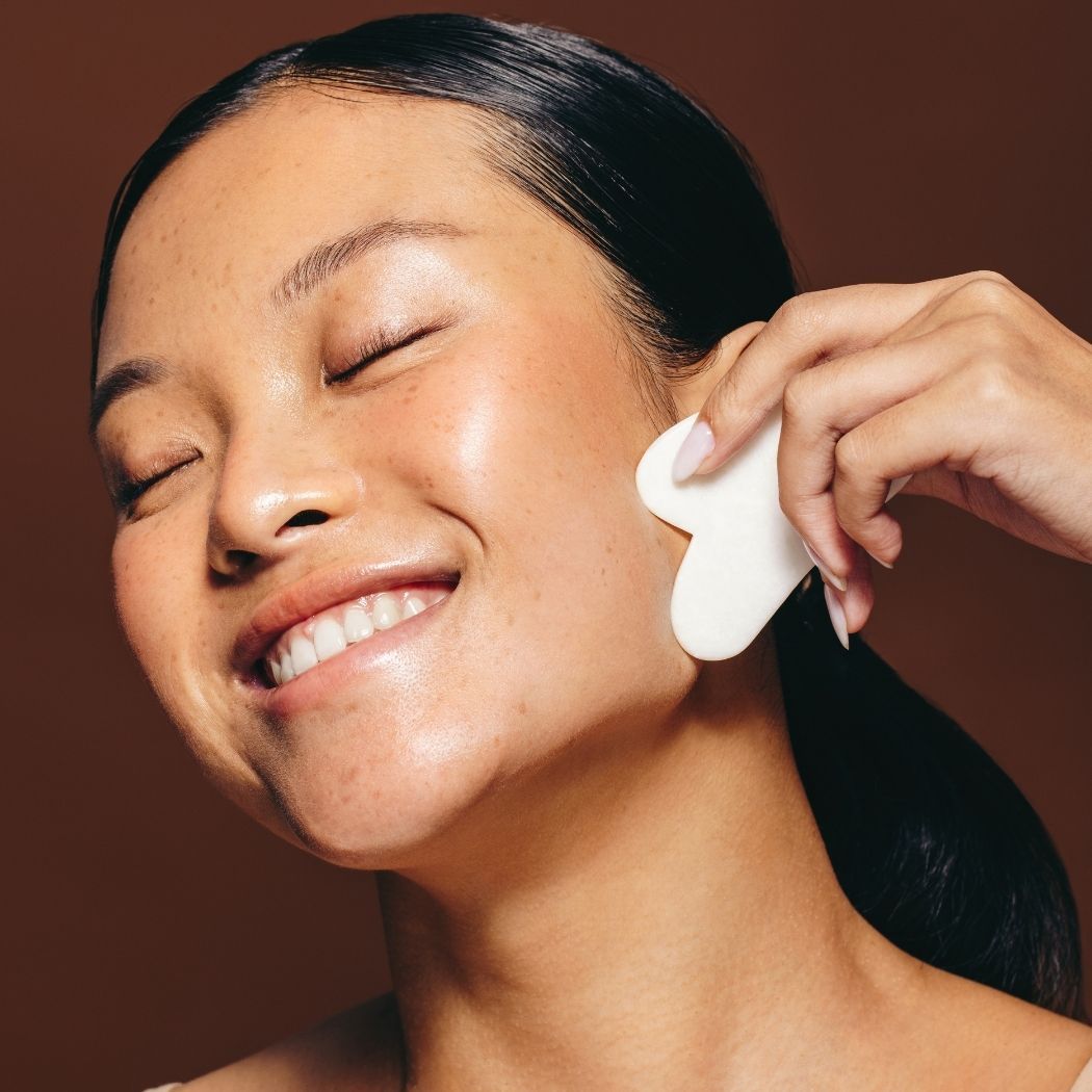 Gua Sha Gesichtsmassage bei Glamskin: eine Frau massiert ihr Gesicht mit einem Gua-Sha-Stein.