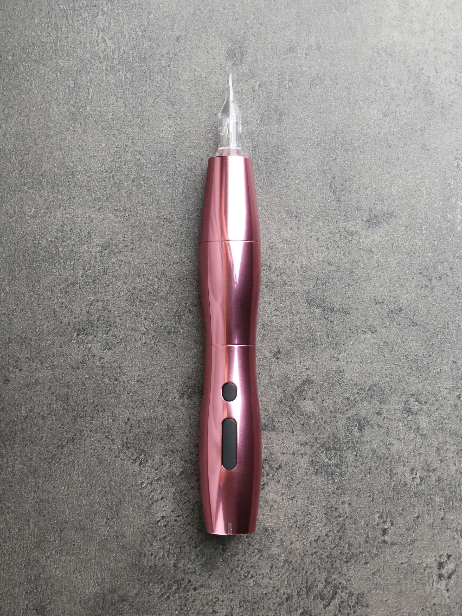 Permanent-Make-up-Gerät von Glamskin in Roségold auf hellem Steinhintergrund.